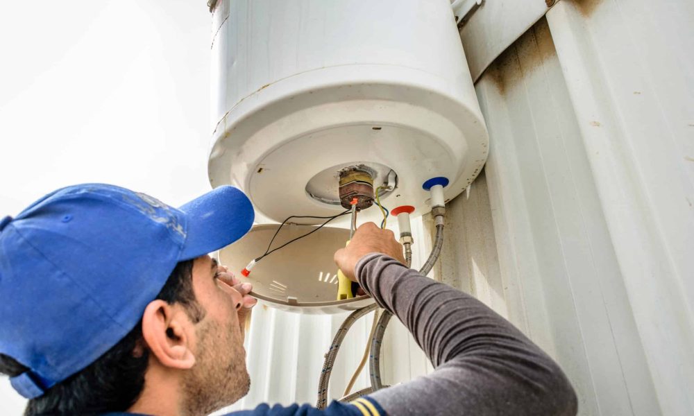 a professional electrician man is fixing a water heater at the roof top and wearing blue uniform and cap