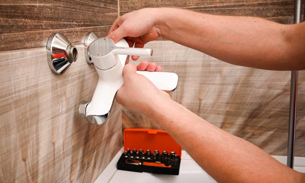 Professional plumber working carefully, installing or repairing bathtub faucet in modern bathroom.