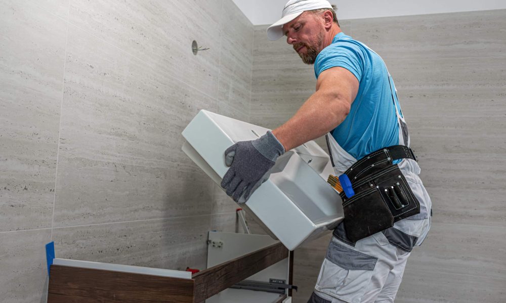 Installation of bathroom furniture. The plumber laying a double washbasin on a cabinet.