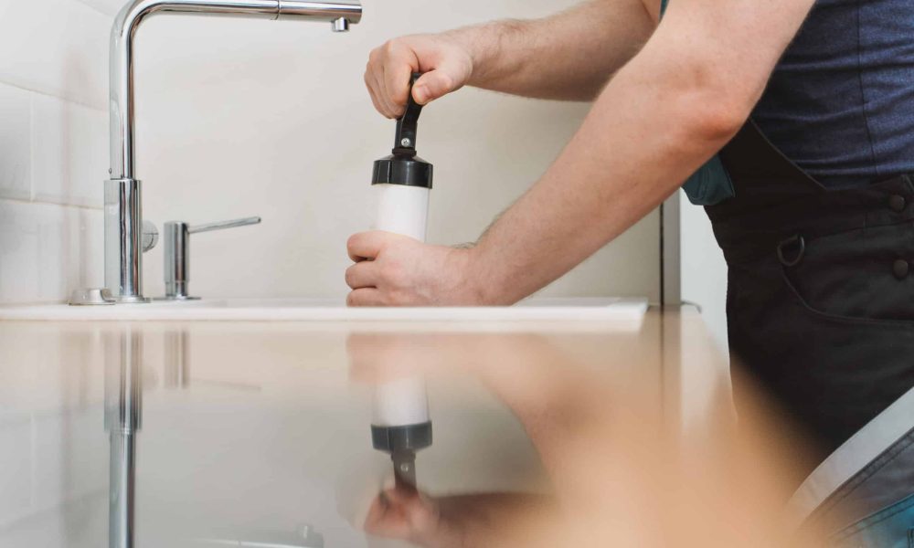 Plumber unclogging kitchen sink with professional force pump cleaner.